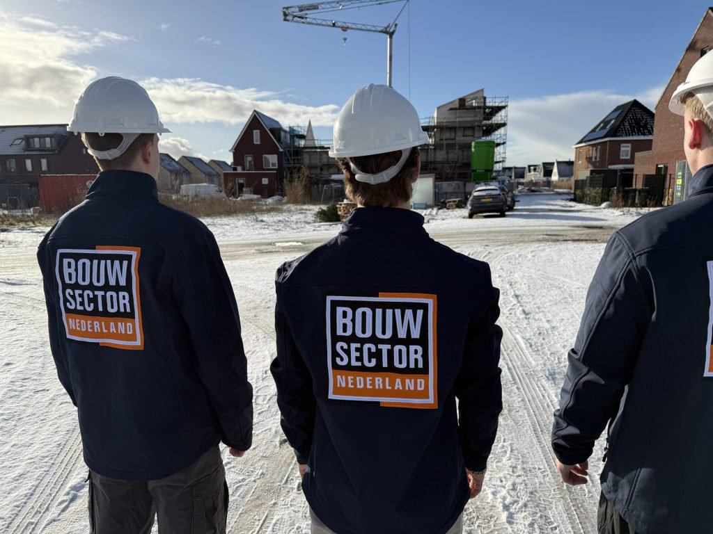 Drie vakmensen van Bouwsector Nederland met witte helm kijken naar nieuwe woningen in de sneeuw